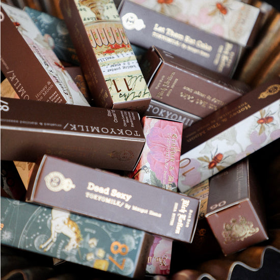 Assorted hand cream tubes by Tokyo Milk, packaged in decorated brown boxes, displayed in a gold ruffled bowl.
