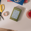 Planner stamp set by Papier, including various icons on a sage green box, with scissors and washi tape nearby.
