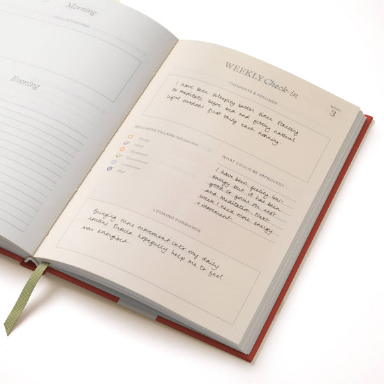 Open guided wellness journal with lined pages by Floral Ikat, showing handwriting and a page marker.