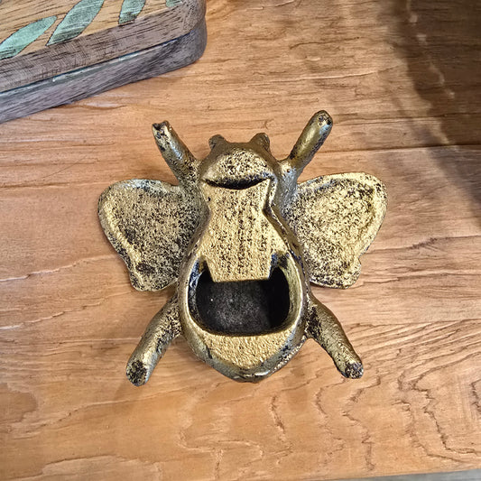 Gold cast iron bee bottle opener with wings on a wooden surface.