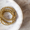 Gold ball bracelet with 8mm beads by unknown brand, styled on a white marble tray with light and dark stone marbling.
