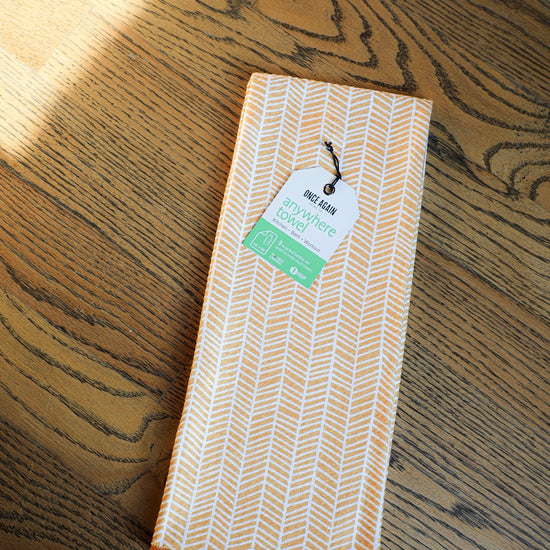 Orange herringbone kitchen towel by Once Again with a tag, on a hardwood floor.