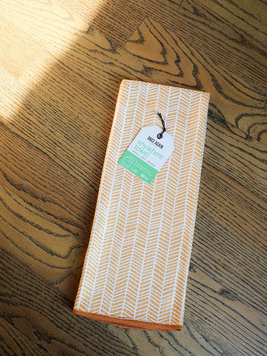 Orange herringbone kitchen towel by Once Again with a tag, on a hardwood floor.