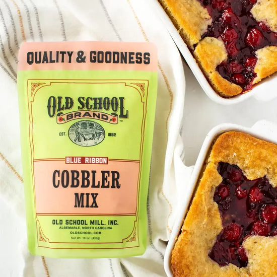 Cobbler mix by Old School Brand alongside two baked cobblers on a striped tea towel.
