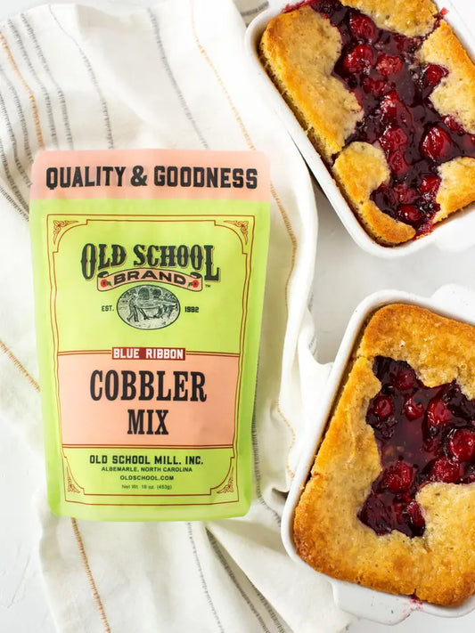 Cobbler mix by Old School Brand alongside two baked cobblers on a striped tea towel.
