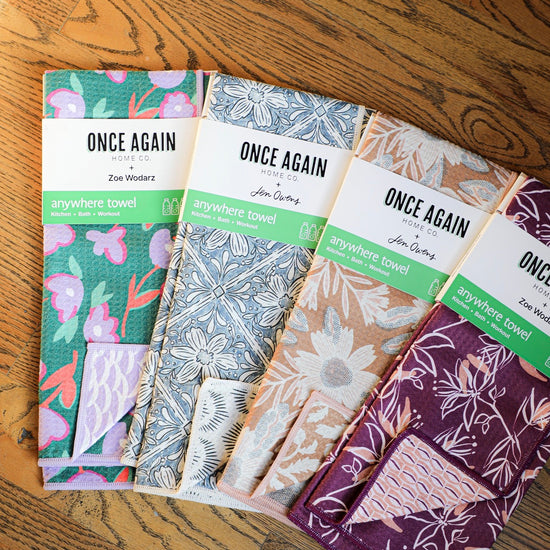 Reusable anywhere towels by Once Again Home Co. with reversible floral patterns and colorful trims, stacked on a wood floor.
