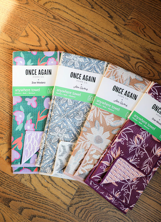 Reusable anywhere towels by Once Again Home Co. with reversible floral patterns and colorful trims, stacked on a wood floor.
