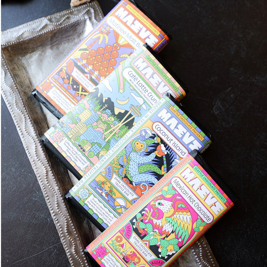 Colorful chocolate truffle bars by Maeve, stacked on a decorative silver tray with a textured handle.
