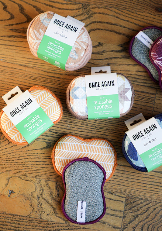 Reusable sponges by Once Again Home Co. in various patterns and colors on a wood surface.

