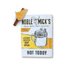 Single serve hot toddy cocktail mix by Noble Mick's, alongside cinnamon stick and honey.
