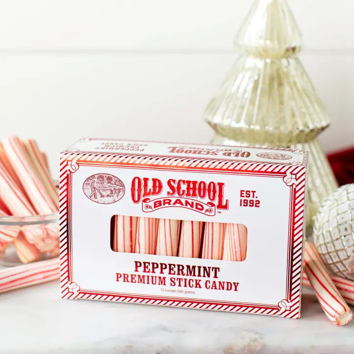 Box of peppermint stick candy by Old School Brand, with festive striped pattern and decorative Christmas ornaments nearby.
