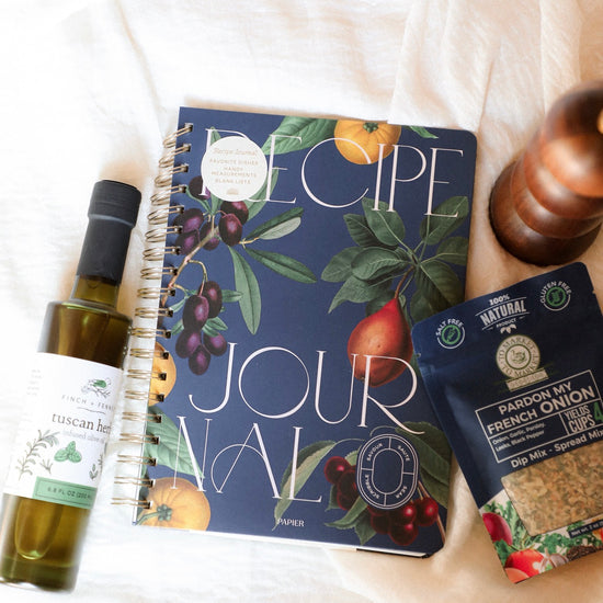 Recipe journal with olive oil bottle and seasoning packet on a white surface