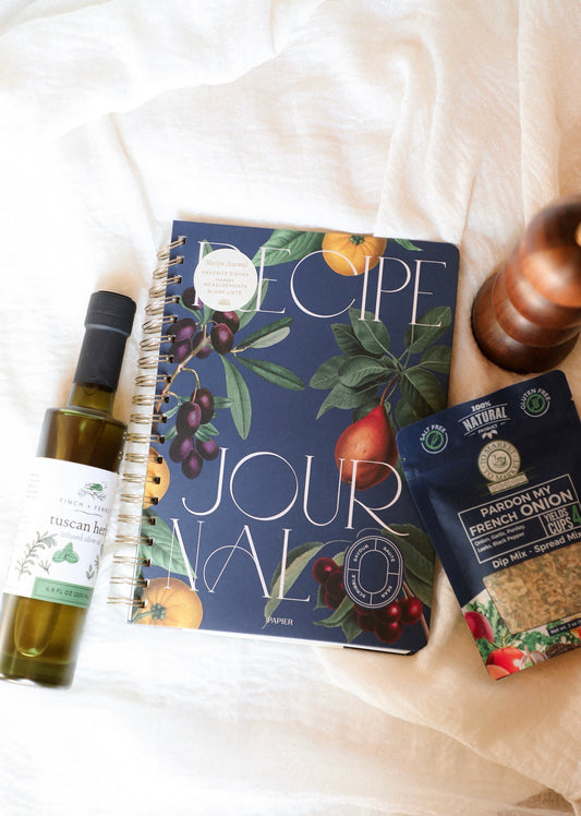 Recipe journal with olive oil bottle and seasoning packet on a white surface