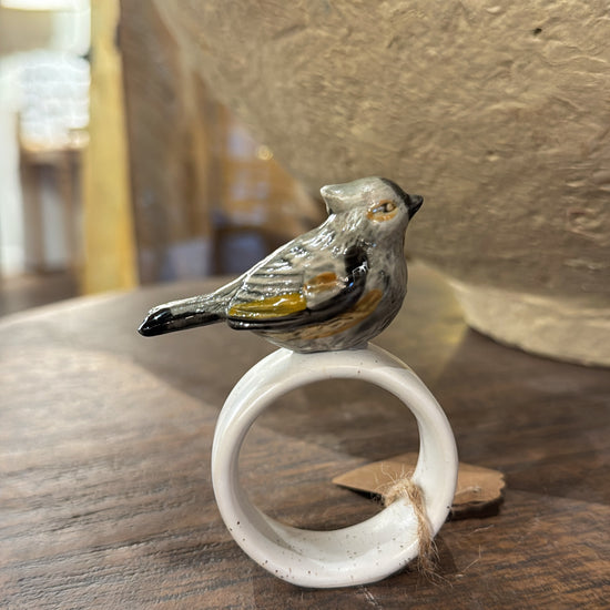 White stoneware napkin ring with a ceramic bird by Creative Co-op, resting on a wood surface.