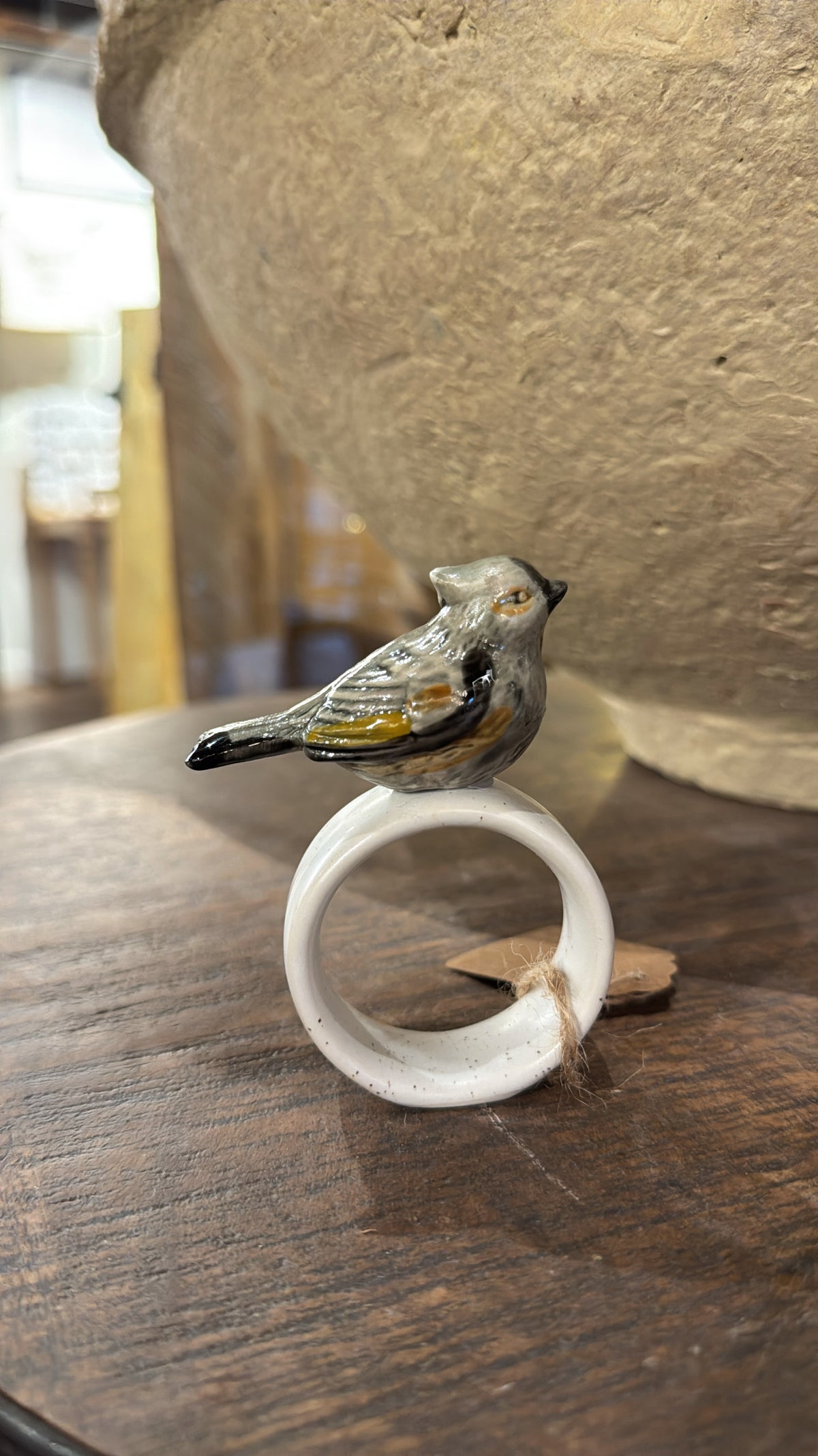 White stoneware napkin ring with a ceramic bird by Creative Co-op, resting on a wood surface.