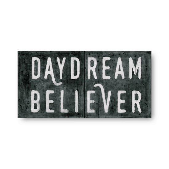 Black and white art tiles with 'Daydream Believer' text, featuring weathered texture.
