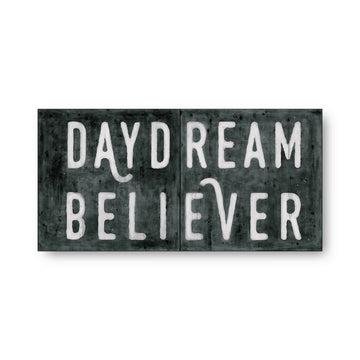 Black and white art tiles with 'Daydream Believer' text, featuring weathered texture.

