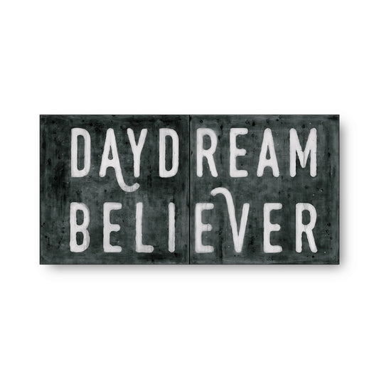 Black and white art tiles with 'Daydream Believer' text, featuring weathered texture.
