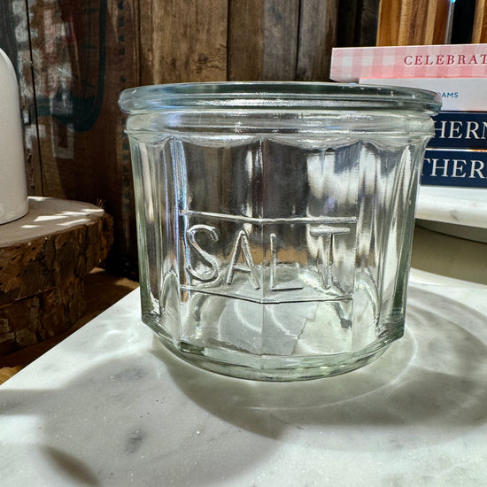 Clear pressed glass salt cellar with “SALT” inscription, on a marble surface.