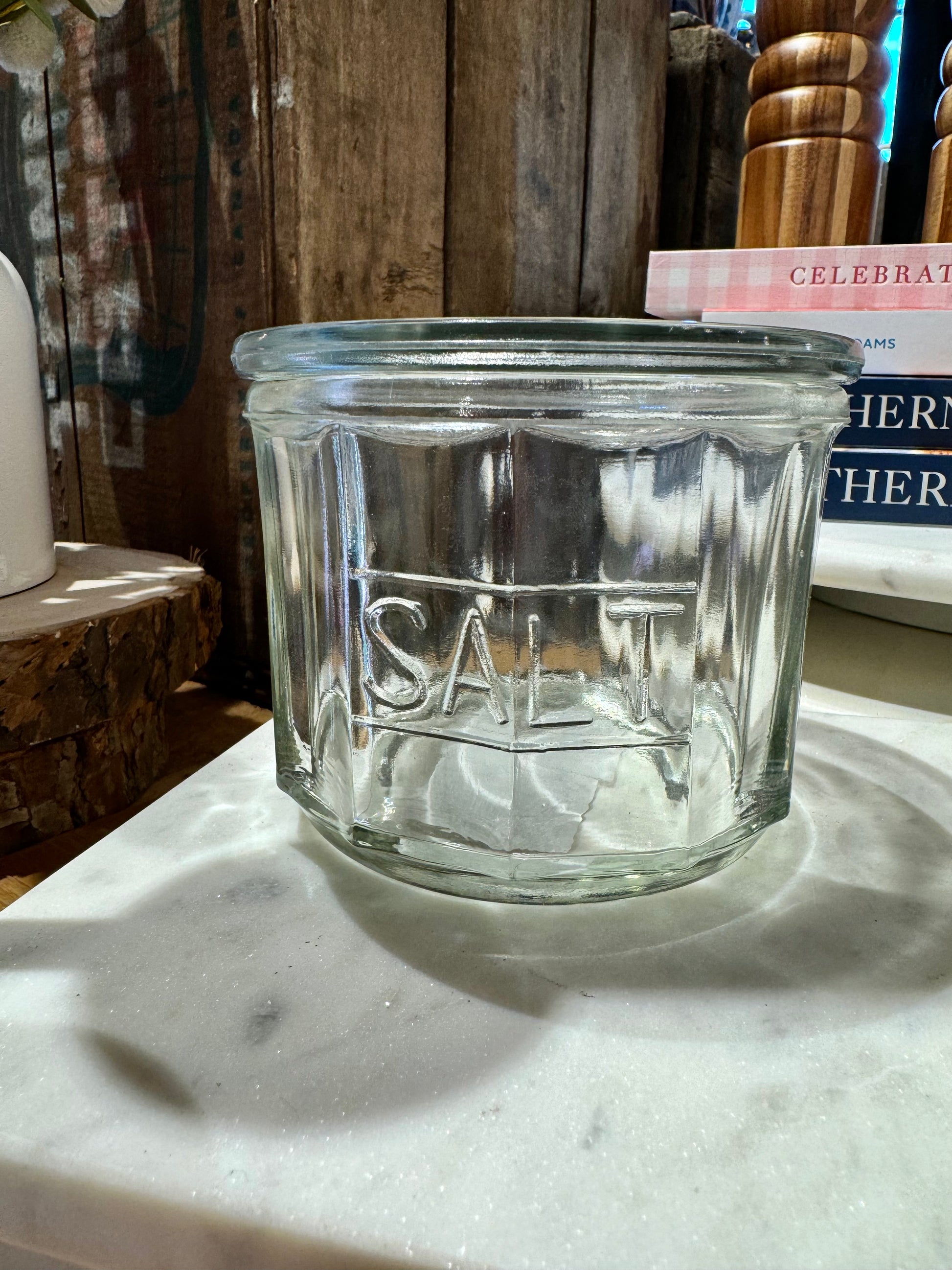 Clear pressed glass salt cellar with “SALT” inscription, on a marble surface.