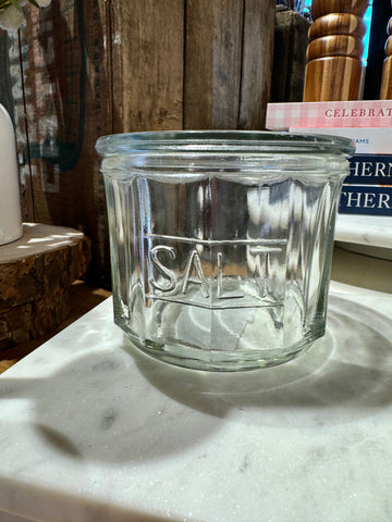 Clear pressed glass salt cellar with “SALT” inscription, on a marble surface.