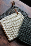 Cotton crocheted pot holders with leather loops, stacked on a wooden table.