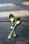 Gold-toned engraved spoons with "tea?" inscription by Creative Brands, arranged on rustic dark wood surface.