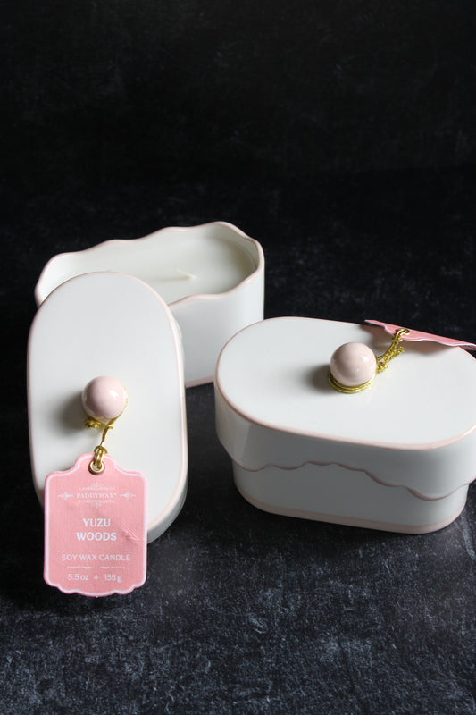 Ceramic candle with lid by Paddywax and a pink gift tag and a golden twine on a dark gray background.