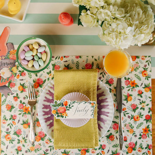 Floral placemat with roses and foliage, from PPD, styled with a plate, napkin, and orange juice in a flat lay.