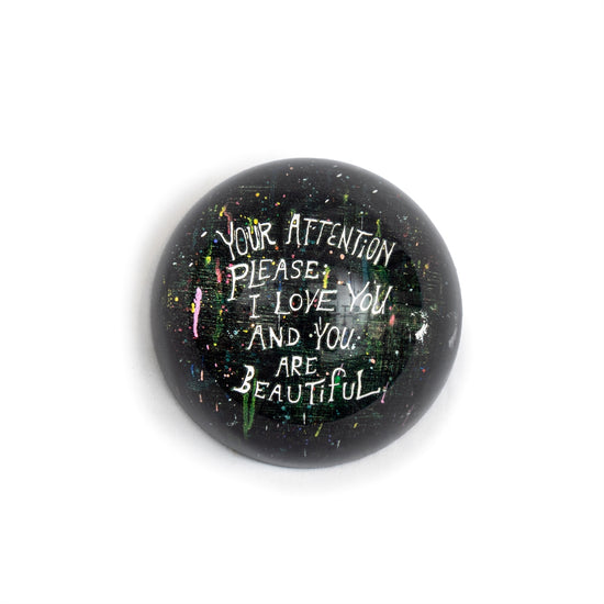 Round paperweight by Sugarboo & Co., featuring splattered colors with a handwritten-style message.
