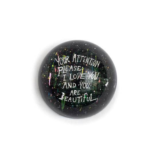 Round paperweight by Sugarboo & Co., featuring splattered colors with a handwritten-style message.
