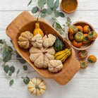 Food safe dough bowl with light brown wood grain, filled with decorative gourds.
