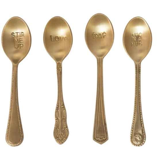 Gold-toned engraved spoons with unique handle designs, each stamped with a different phrase.