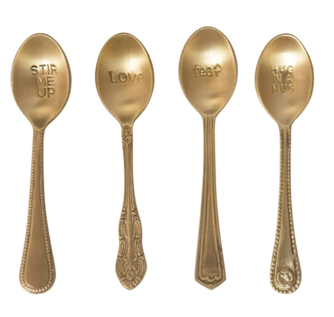 Gold-toned engraved spoons with unique handle designs, each stamped with a different phrase.