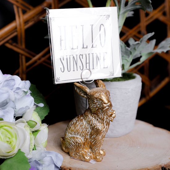 Gold resin bunny place card holder with metal spring clip, holding a card with flowers on a wood slice.