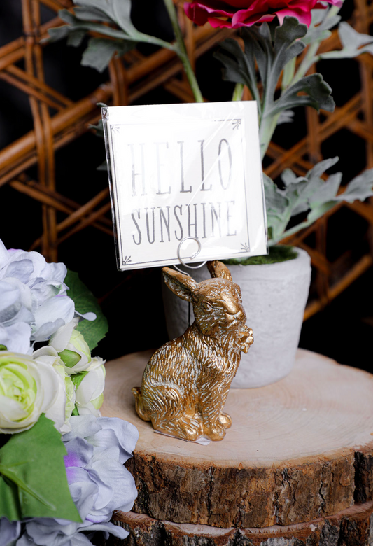 Gold resin bunny place card holder with metal spring clip, holding a card with flowers on a wood slice.