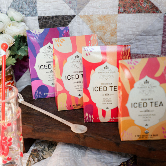 Four packages of 'ICED' iced tea on a wooden surface with a quilted fabric background.