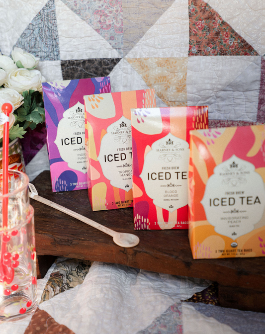 Four packages of 'ICED' iced tea on a wooden surface with a quilted fabric background.