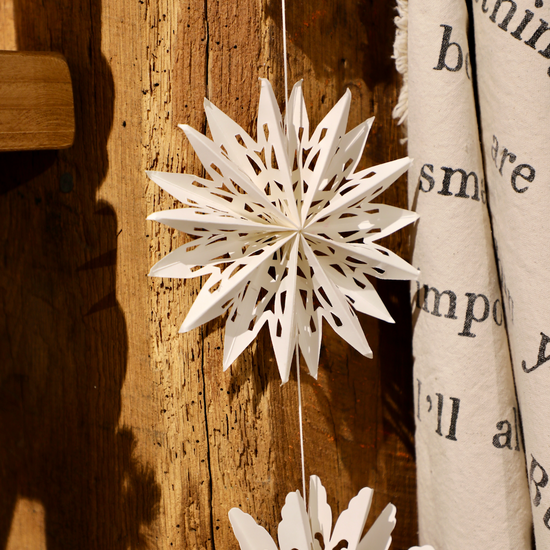 White snowflake garland for Christmas, with paper cutouts, hanging from a rustic wooden surface.