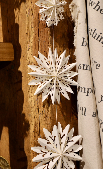 White snowflake garland for Christmas, with paper cutouts, hanging from a rustic wooden surface.
