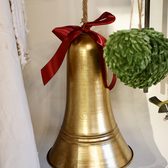 Antique golden bell by Carillon, adorned with a red ribbon, hangs from a jute rope near colorful decorative eggs.