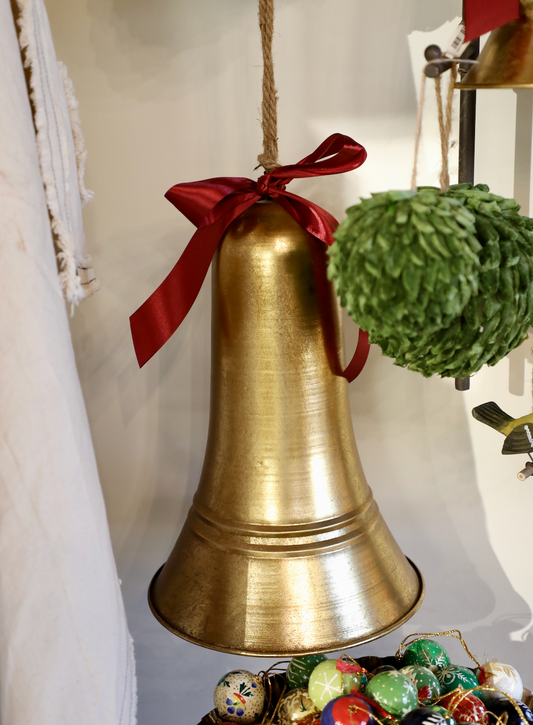 Antique golden bell by Carillon, adorned with a red ribbon, hangs from a jute rope near colorful decorative eggs.