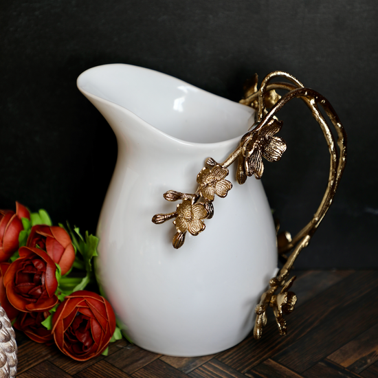 White pitcher with gold handle from The-Little-Shop-Of-Gifts, featuring a decorative floral motif and elegant styling.
