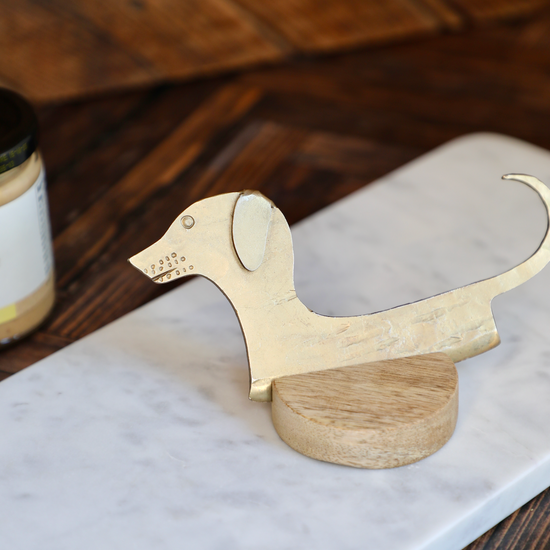 Hand-forged dachshund cheese knife on a wooden base, with a marble board background.