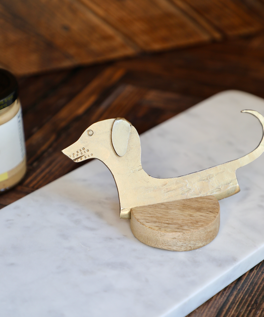 Hand-forged dachshund cheese knife on a wooden base, with a marble board background.