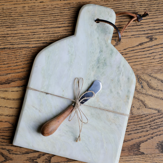 Marble cheese board with canape knife, tied with twine, on a wood surface.

