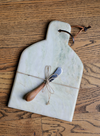 Marble cheese board with canape knife, tied with twine, on a wood surface.
