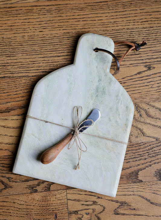Marble cheese board with canape knife, tied with twine, on a wood surface.
