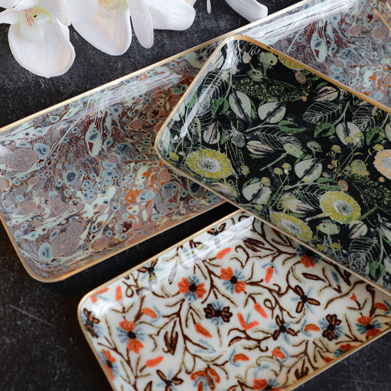 Decorative enameled metal trays with gold rims featuring floral patterns and marble-like textures.
