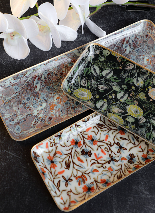 Decorative enameled metal trays with gold rims featuring floral patterns and marble-like textures.